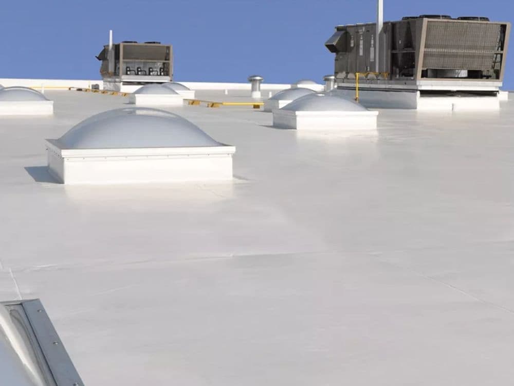 Commercial building roof featuring skylights and HVAC units against a clear blue sky.